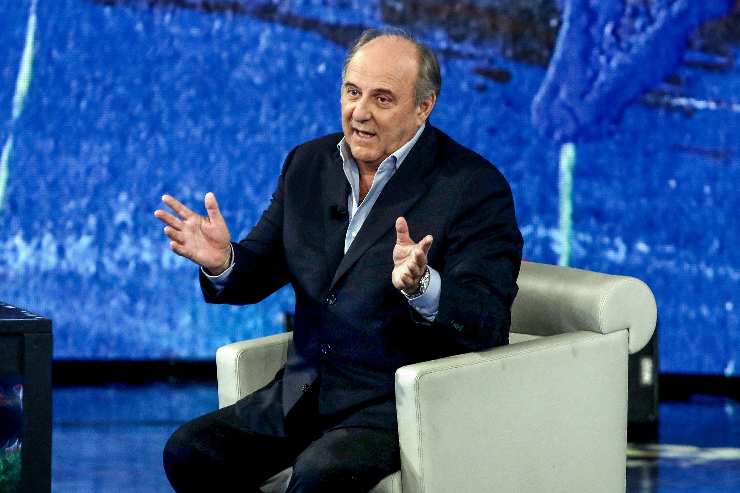gerry scotti seduto allarga le braccia